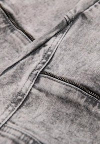 Acercamiento a una tela de denim gris desgastado con un zipper metálico expuesto parcialmente abierto a lo largo de una costura.
