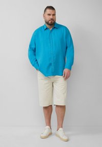 Lichtblauwe linnen overhemd met knopen, beige shorts en witte sneakers. Het overhemd heeft lange mouwen en een relaxte pasvorm. Minimalistisch ontwerp.