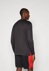 Black long-sleeve shirt with a round neckline, paired with black shorts featuring red side accents. Both items are made from lightweight fabric.