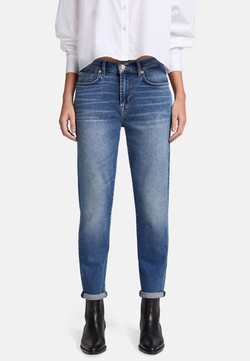 Jeans skinny in denim blu medio, con finitura sbiadita, orli arrotolati e styling a cinque tasche, abbinati a una camicia bianca con bottoni.
