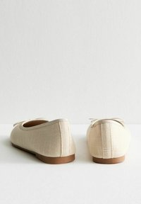 Bailarinas beige hechas de un tejido texturizado, con una suela plana y un detalle de cordones minimalista en la parte delantera, con un forro interior suave.