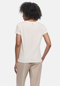 Weißes Kurzarm-T-Shirt mit rundem Ausschnitt und einem kleinen Akzentknopf am Rücken. Weiches Baumwollmaterial mit glatter Textur.