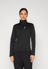 Maglione in pile nero con zip e colletto alto, caratterizzato da un pannello testurizzato sul petto e maniche lunghe aderenti. Branding minimale nella zona del petto.
