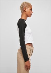 Sort og hvid cropped langærmet skjorte med en tætsiddende pasform; sorte ærmer står i kontrast til en hvid krop. Sammen med beige bukser.