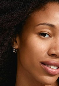 Orecchino a cerchio in argento con un design scultoreo, caratterizzato da una superficie testurizzata e un piccolo dettaglio decorativo. Indossato su un orecchio con capelli naturali.