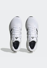 Scarpe sportive bianche con tomaia testurizzata, strisce nere e lacci. Punta arrotondata e suola imbottita con un logo distintivo sulla soletta.