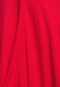 Czerwona tkanina o gładkiej fakturze, z miękkimi fałdami i subtelnym połyskiem. Materiał wydaje się lekki i elastyczny.