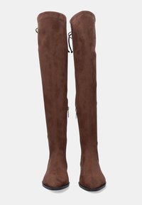 Botas de ante marrón, por encima de la rodilla, con cremalleras laterales y cierres de lazo en la parte superior, exhibidas de pie sobre un fondo liso.