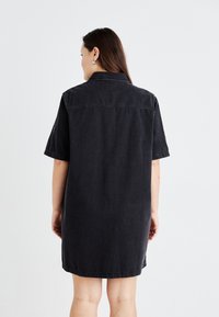 Zwarte denim jurk met korte mouwen, een kraaghalssluiting en een rechte pasvorm. Heeft een rugpand en subtiele stikdetails.