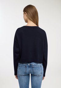 Maglione corto blu navy con orlo a coste e spalle larghe e scese. Indossato con jeans denim azzurri. Materiale a maglia liscia e strutturata.