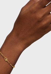 Złota bransoletka z łańcuszkiem o fakturowanym wzorze ogniw i zapięciem na hak, prezentowana na ręce o brązowej karnacji.