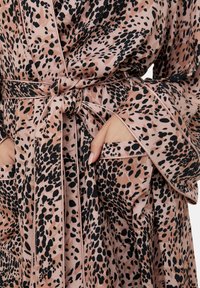 Silk robe featuring a pink base with black irregular spots, a wrap design, wide sleeves, and a tied waist belt with pocket detailing.