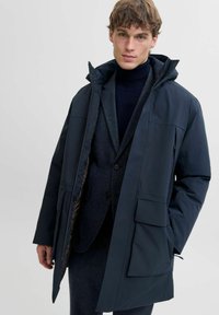 Tamsiai mėlynas parka tipo švarkas su kapišonu, turintis kelias kišenes ir užtrauktuko uždarymą. Pagamintas iš sklandžios, vandeniui atsparios medžiagos su užpildyta pamušalu.