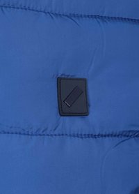 Blauwe opblaasjack stof met geplooide textuur. Heeft een rechthoekig zwart patch met een geometrische accent. Glad materiaal, lichtgewicht ontwerp.