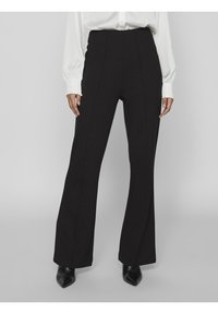 Svarta högmidjade byxor med vid benform, med vertikala sömmar och en slät textur. Kombination med en vit blus och svarta klackar.