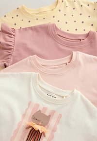 Cztery złożone dziecięce topy w pastelowym żółtym kolorze z fioletowymi kropkami, jednolite w kolorze przydymionego różu, jasnej brzoskwini oraz białe z grafiką kota i falbanami.