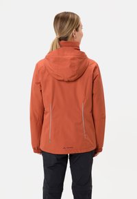 Giacca impermeabile rosso-arancio con cappuccio, dotata di due cerniere laterali e lacci regolabili, progettata per l'uso all'aperto.