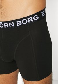 Schwarze Baumwollboxershorts mit einem schwarzen Bund, der mit weißen "BJÖRN BORG"-Markierungen versehen ist. Der Stoff ist glatt und hat kontrastierende Nähte.