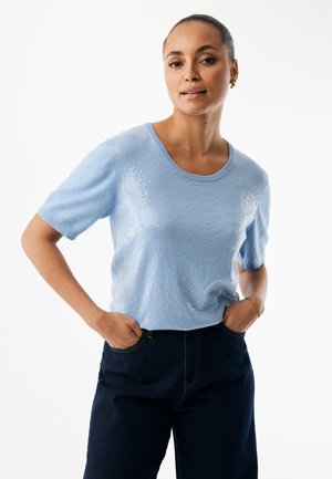 Jasnoniebieski sweter z krótkim rękawem o miękkiej teksturze i połyskujących akcentach. Okrągły dekolt i luźny krój, zestawiony z ciemnymi spodniami dżinsowymi.