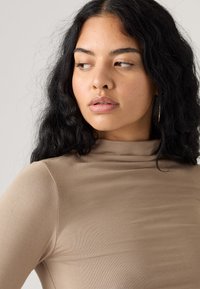 Barna turtleneck felső sima, rugalmas anyagból, testhezálló fazonban, finom redőzéssel a nyakrészen.
