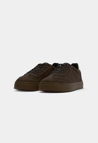 Brown suede sneakers with a rounded toe, flat lace-up design, and rubber sole. Features subtle stitching details and a contrasting heel accent.