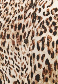 Leoprintstoff mit braunen und schwarzen Flecken auf beigem Hintergrund, mit einer Reihe dunkelbrauner Knöpfe.