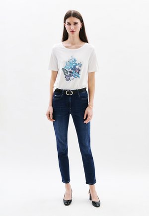 T-shirt blanc à manches courtes avec un motif floral bleu, associé à un jean skinny en denim bleu foncé et des chaussures à talons hauts noires.