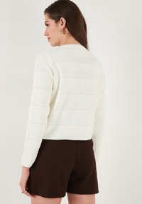 Gestreifter Cremefarben Pullover mit Rippstruktur und langen Ärmeln, kombiniert mit braunen Shorts. Verfügt über einen runden Ausschnitt und ein kurzes Design.
