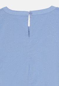 Blouse bleu clair avec un motif texturé, une ouverture en forme de goutte d'eau à l'arrière avec fermeture par bouton, et un design simple et épuré.