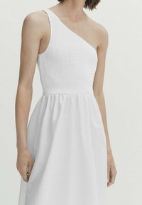 Abito bianco con un spallaccio, caratterizzato da un corpetto arricciato e una gonna fluida e strutturata. Texture liscia, design semplice ed elegante silhouette.