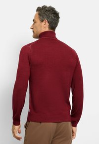 Burgunderfarbener, langärmeliger Rollkragenpullover mit geripptem Kragen und Bündchen, aus weichem Stoff. Seitlicher Schlitzakzent in der Nähe des Saums.