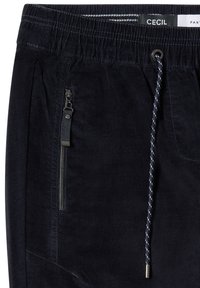 Granatowe spodnie z korduroju z elastycznym pasem, sznurkiem i szczegółami w postaci kieszeni zapinanej na zamek. Gładka tekstura i swobodny design.