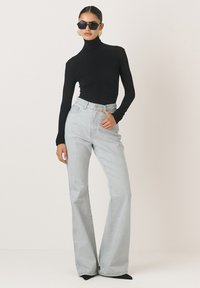 Juodas golfo tipo megztinis derinamas su šviesiai mėlynomis aukšto liemens plačiomis džinsomis. Džinsai turi knopkę ir šonines kišenes.