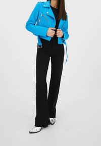 Světlá modrá kožená bikerská bunda s asymetrickými zipy, doplněná o černé rozšiřující se kalhoty a stříbrné boty s špičatou špičkou.