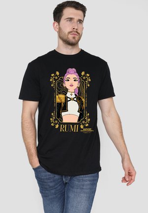 Man wearing black T-shirt with illustrated pink-haired woman in gold and white jacket framed by floral design and text "RUMI" and "KPOP DEMON-HUNTERS."