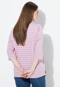 Rosa och blå randig topp med trekvartslånga ärmar, avslappnad passform, slät tyg och sidoförsedda slitsar i nederkant, bärs med blå jeans.