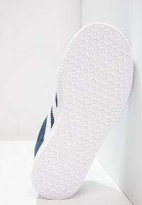 Marineblå sneaker med en texturerad vit gummisula, som har en ren design och kontrasterande sidostrippar i vitt.