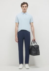 Polo di colore blu chiaro con una patta a due bottoni, pantaloni aderenti blu navy, sneakers bianche e una borsa in pelle nera con doppi manici.