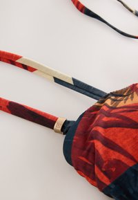 Kolorowy top od bikini z abstrakcyjnym wzorem w czerwono-niebieskich barwach, z regulowanymi ramiączkami i złotym akcentem w miejscu łączenia ramiączek.