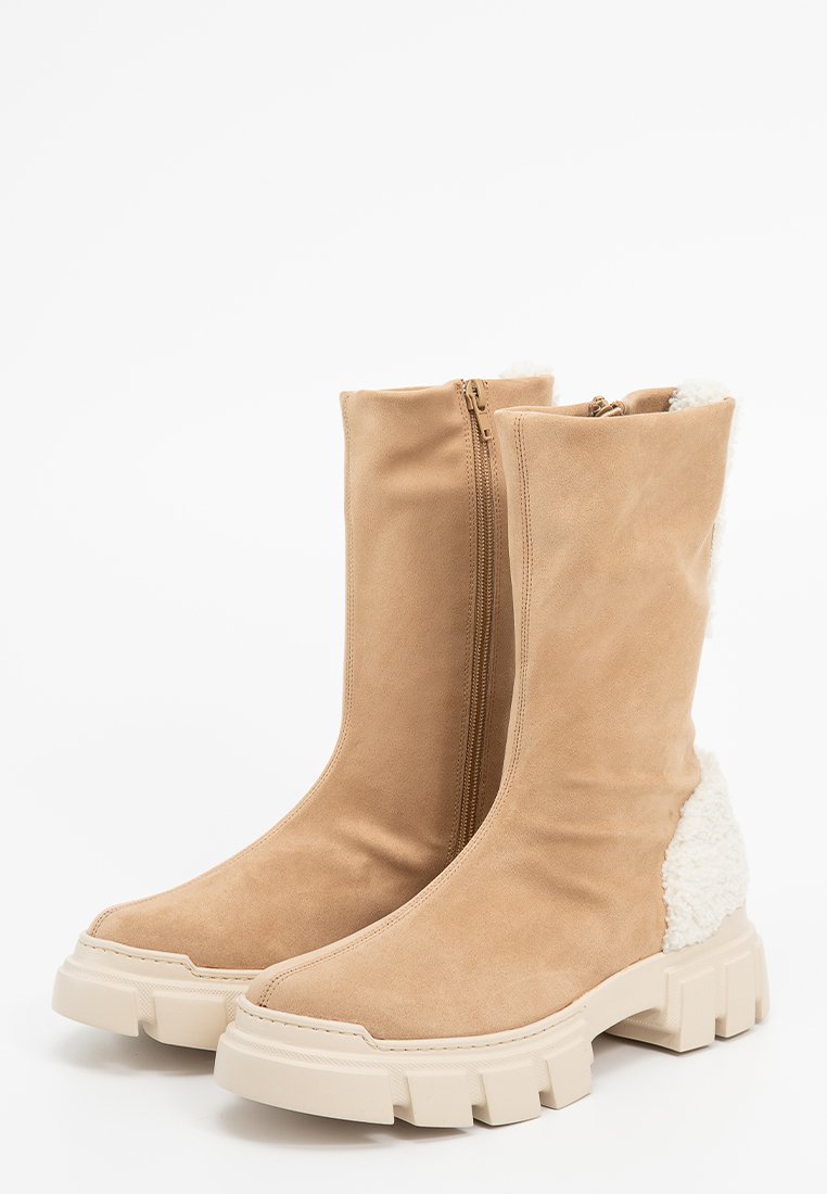 Botas de tobillo de ante beige con un ajuste ceñido, cierre de cremallera y detalles de pelo sintético texturizado en la parte posterior. Suelas de goma blanca gruesa.