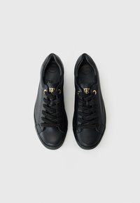 Baskets noires en cuir texturé avec des lacets noirs plats, œillets dorés et bout rond. Présente une semelle intérieure embossée "SUPER SOFT".
