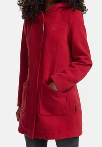 Cappotto in pile rosso con cappuccio, dotato di zip frontale, due tasche anteriori e logo ricamato. Texture liscia con vestibilità comoda.