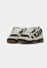 White and black sneakers with a suede and mesh upper, featuring a rubber sole, perforated details, and a prominent logo on the side.