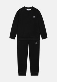 Fekete sportos tréningruha, amely egy kerek nyakú pulóverből és azzal megegyező nadrágból áll, mindkettő fehér Adidas logóval díszítve és bordás mandzsettákkal.