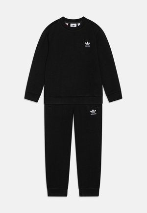 Juodas sportinis treningas, kuriame yra megztinis su apvalia apykakle ir rausvos rankovėmis, taip pat atitinkantys kelniai, abu su baltais Adidas logotipo akcentais.