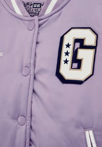 Šviesiai violetinė bomber jaketė su dideliu siuvinėtu "G" ženkliuku ir penkiomis žvaigždėmis, mygtukais snap, dryžuotu elastiniu apykakle ir lygia tekstūra.