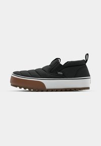 Svart slip-on sko med quiltet overdel, hvit mellomsolette og brun gummisåle. Har en liten logo og en trekklapp for enkel påkledning.