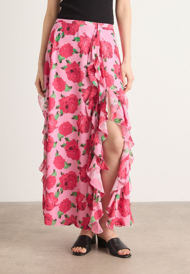 Jupe maxi florale rose avec des volants sur le côté et l'ourlet, ornée de grandes roses rouges et de feuilles vertes, fabriquée en tissu léger.