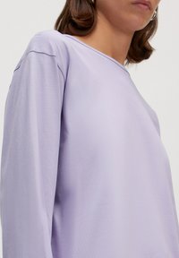 Lila langarmlige shirt met een gladde textuur, voorzien van een ronde hals en subtiele stiksels op de schoudernaden.