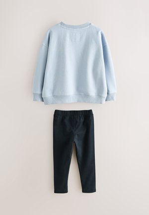 Hellblauer Pullover mit gerippten Bündchen an Ärmeln und Saum, kombiniert mit schwarzen Leggings mit elastischem Bund. Beide aus glatten, strapazierfähigen Stoffen, ordentlich arrangiert.